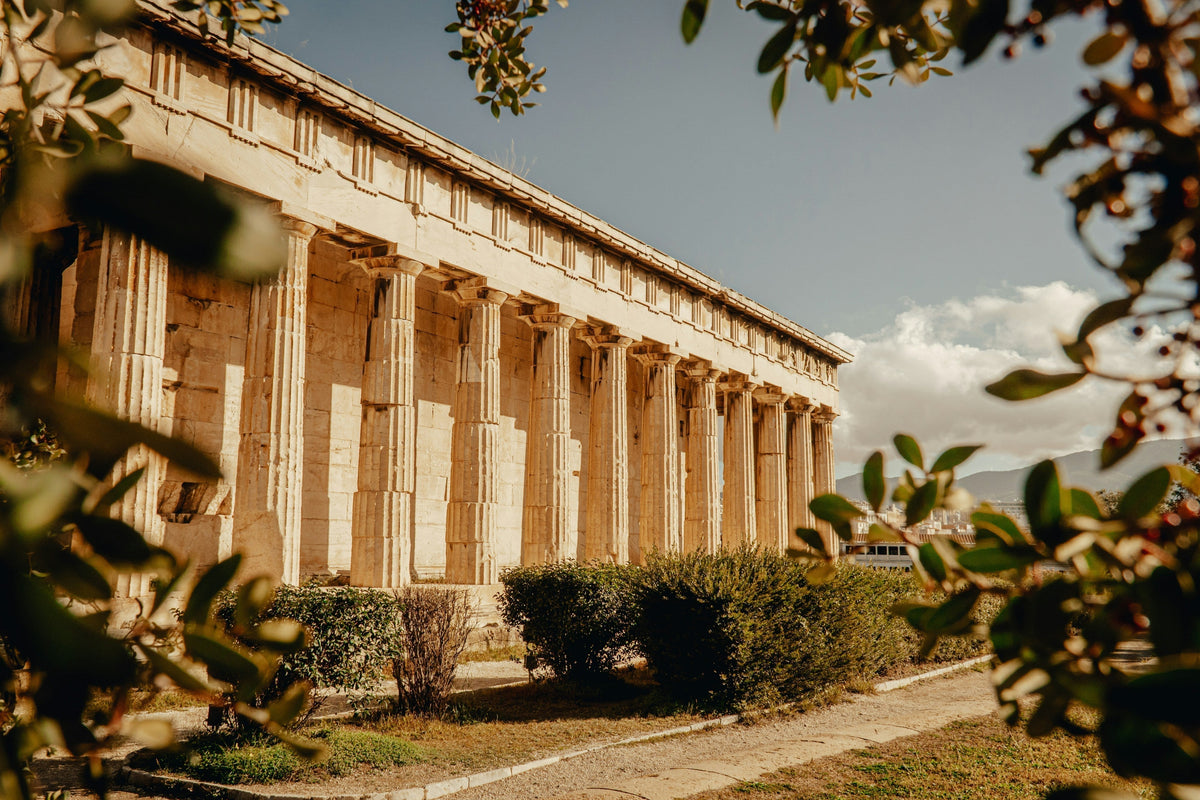 Classical Greek temple surrounded by greenery under a sunny sky.