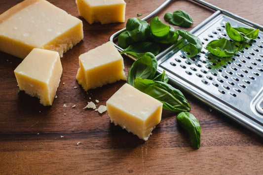 Cubes of hard cheese with fresh basil leaves and a grater on a wooden surface.