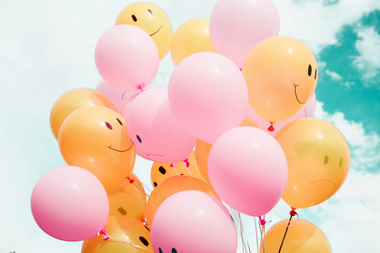 Cluster of pink and yellow balloons with happy and sad faces drawn on them.