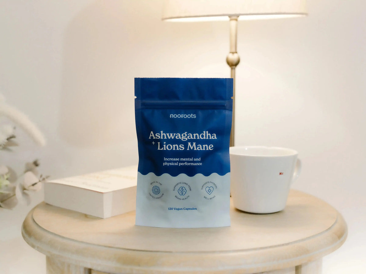 A pouch of Nooroots Ashwagandha + Lion's Mane on a bedside table next to a mug and a book