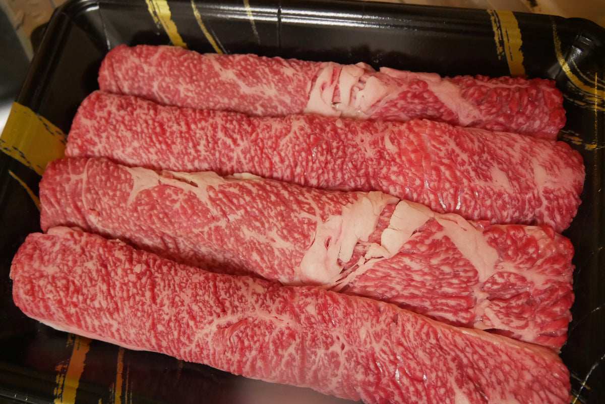 Four rolled slices of raw marbled beef in a tray