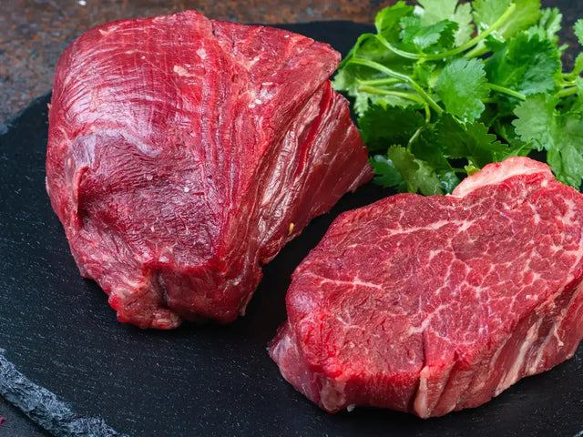 Two cuts of raw red beef on a slate board