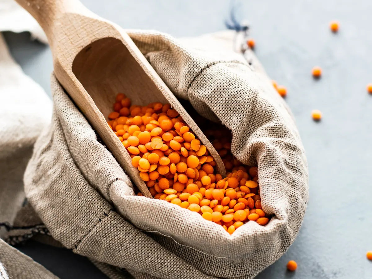 Red lentils spilling from a sack with a wooden scoop
