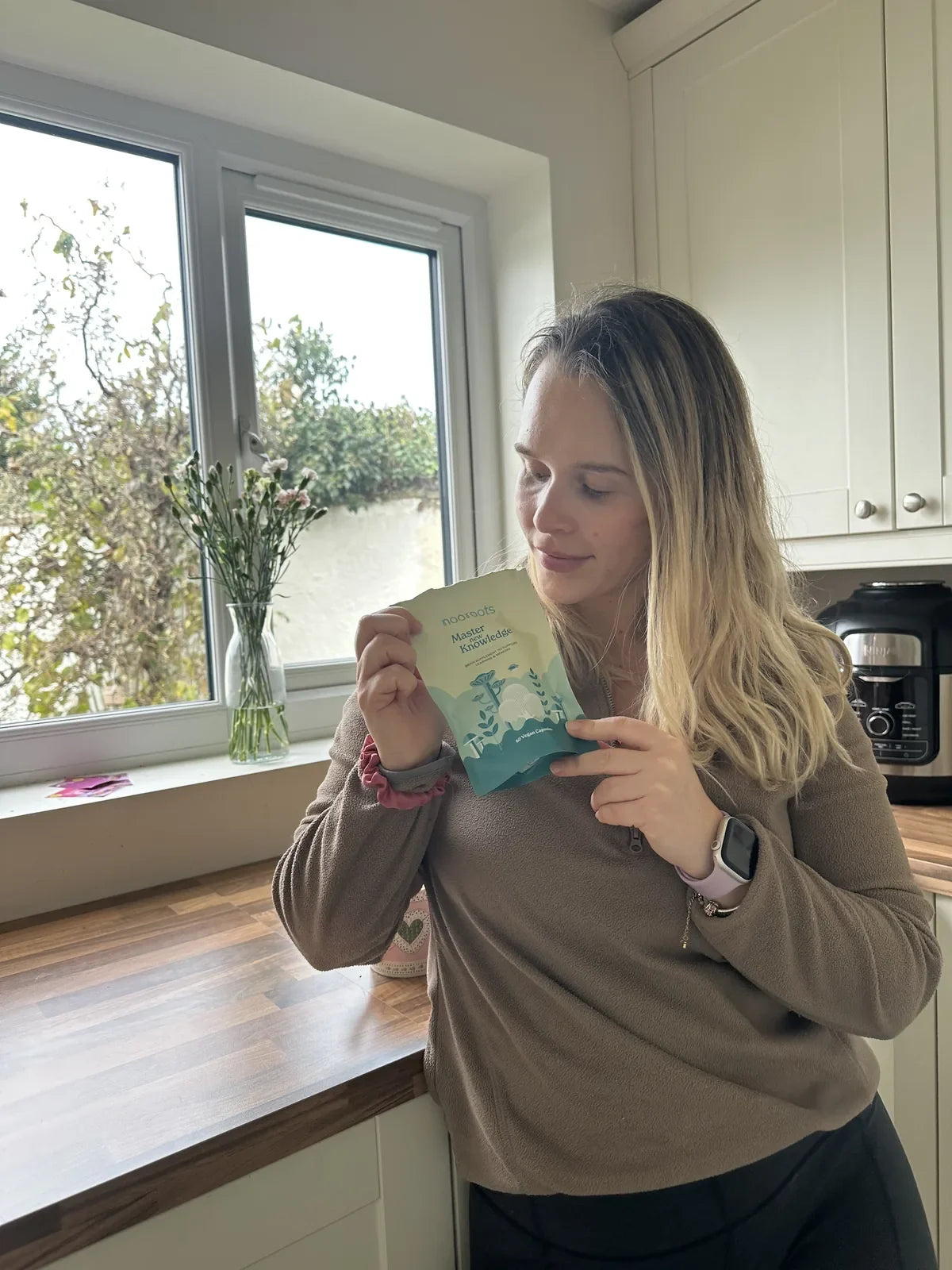 A woman by a bright kitchen window holding a pouch of Learning & Memory