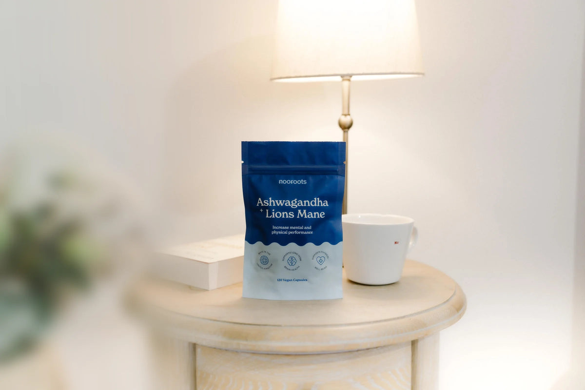 A pouch of nooroots Ashwagandha & Lion's Mane on a bedside table next to a lamp, a book and a mug