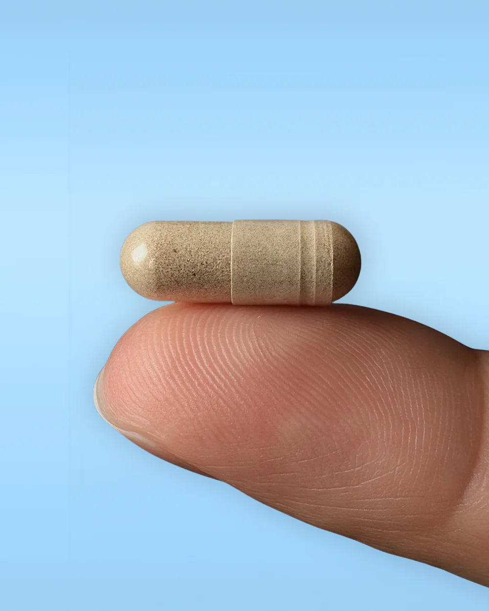 A single capsule resting on a fingertip against a soft blue background