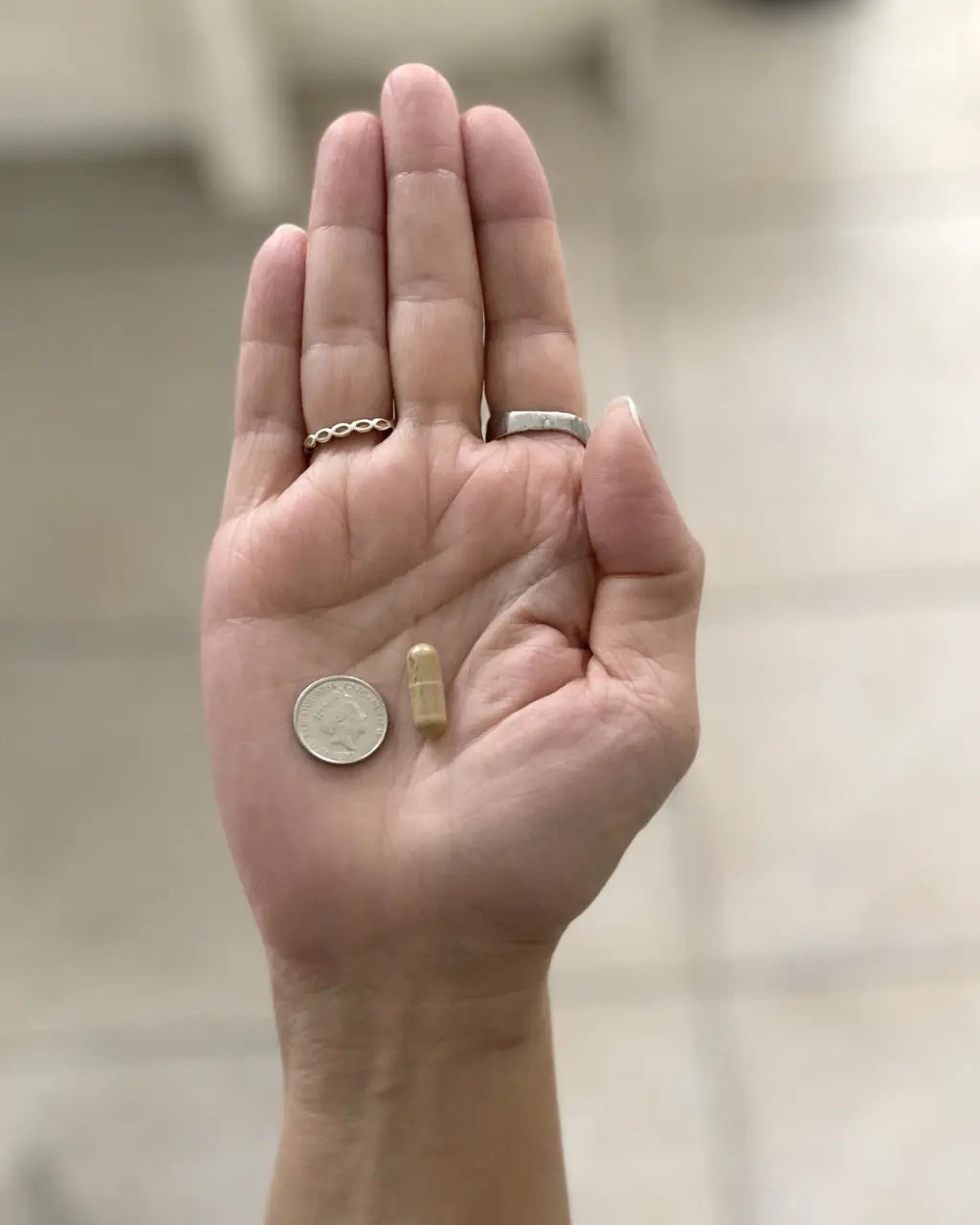 Woman holding a capsule in her hand next to a coin for size comparison