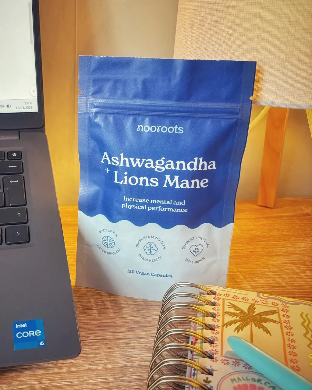 Nooroots Ashwagandha and Lions Mane supplement pouch on a desk beside a notebook and laptop