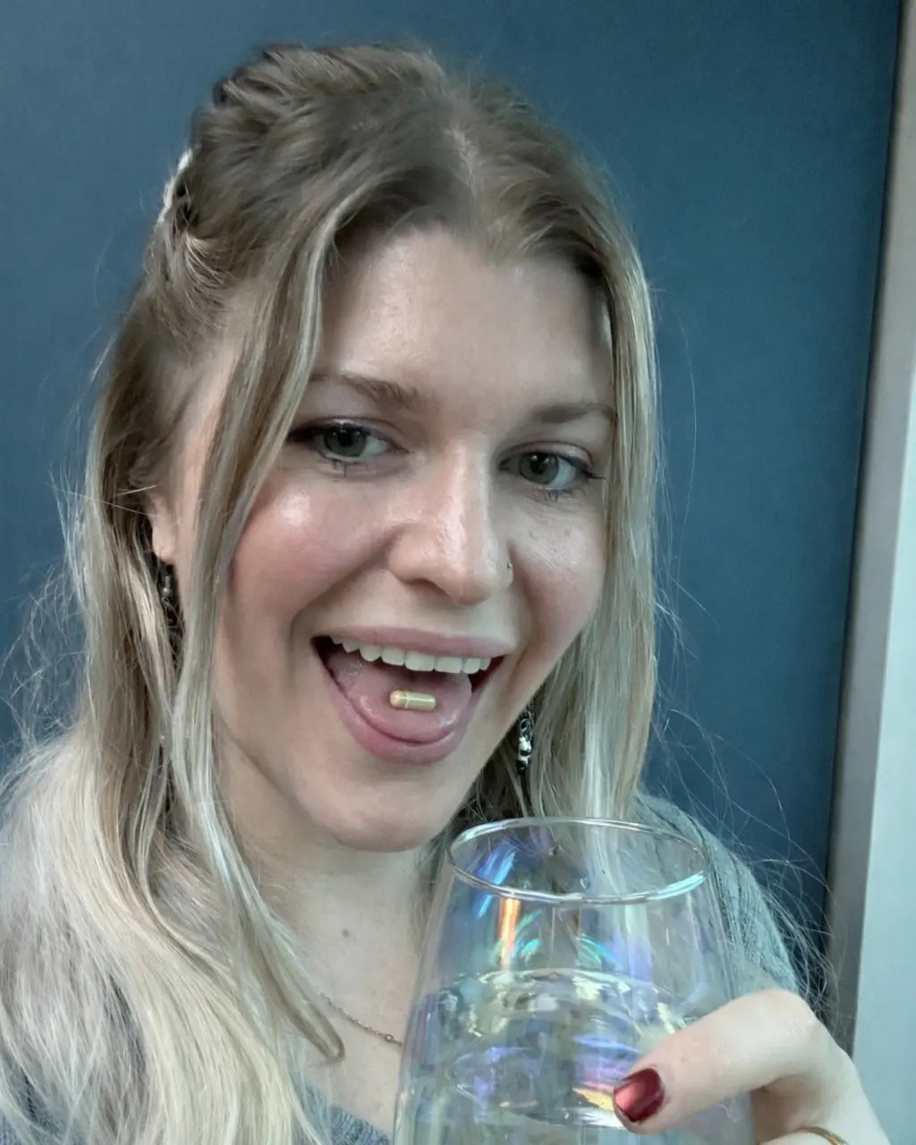 Woman holding a glass of water with a supplement capsule on her tongue